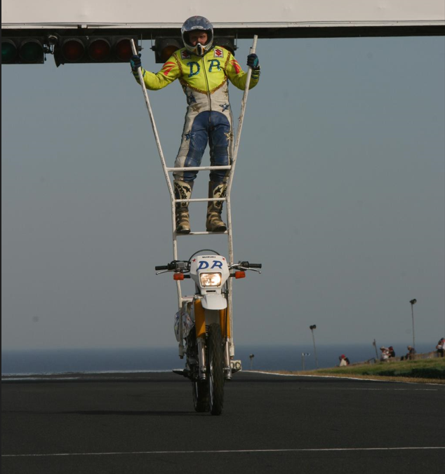 David Russell riding a ladder on a moving motorcycle.